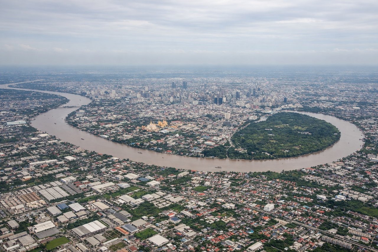 Left window seat view during takeoff from Bangkok (BKK) — Chao Phraya River bends, Bangkok skyline and skyscraper clusters, Suvarnabhumi's surrounding canals and wetlands, dense urban sprawl of greater Bangkok