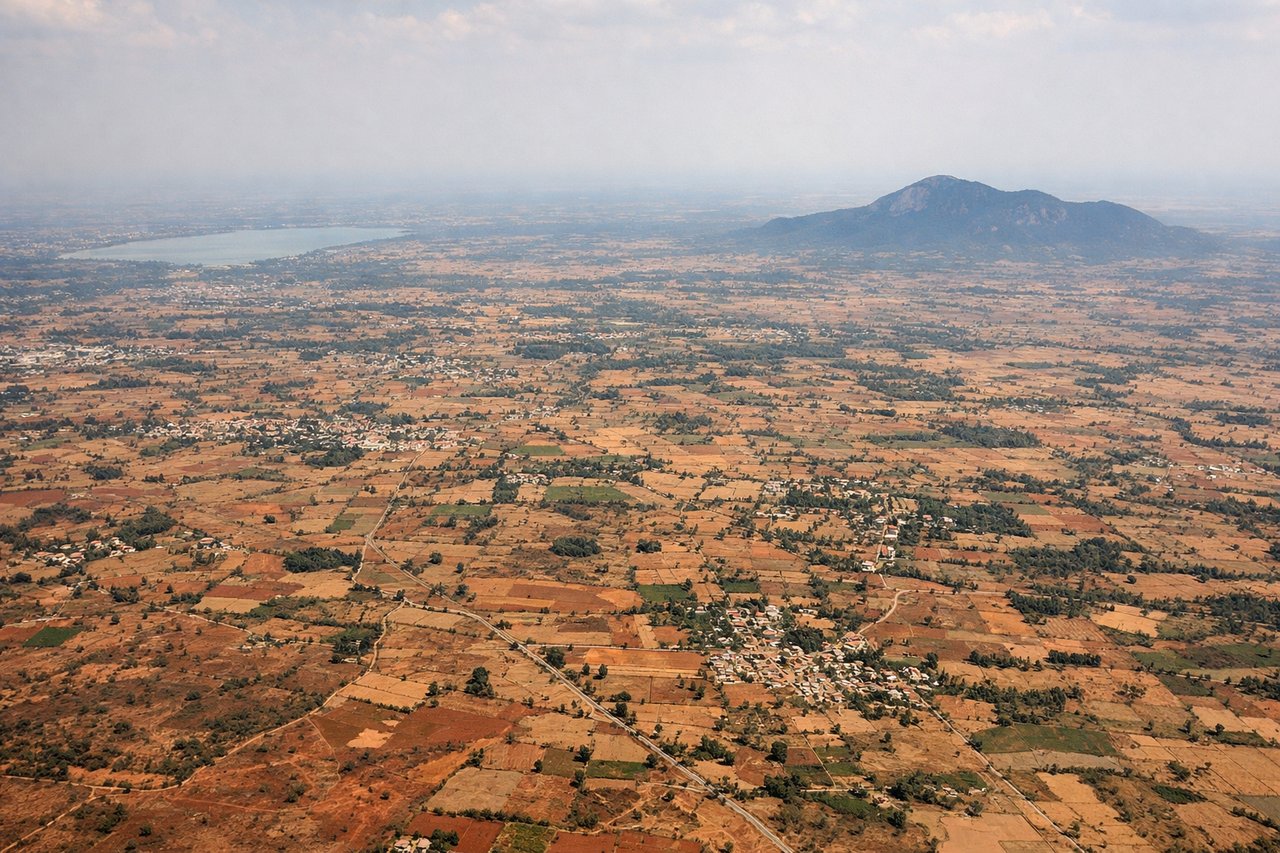 Right window seat view during takeoff from Bangalore (BLR) — Nandi Hills, Devanahalli town near the airport, scattered irrigation tanks/lakes on the Deccan plateau, patchwork farmland