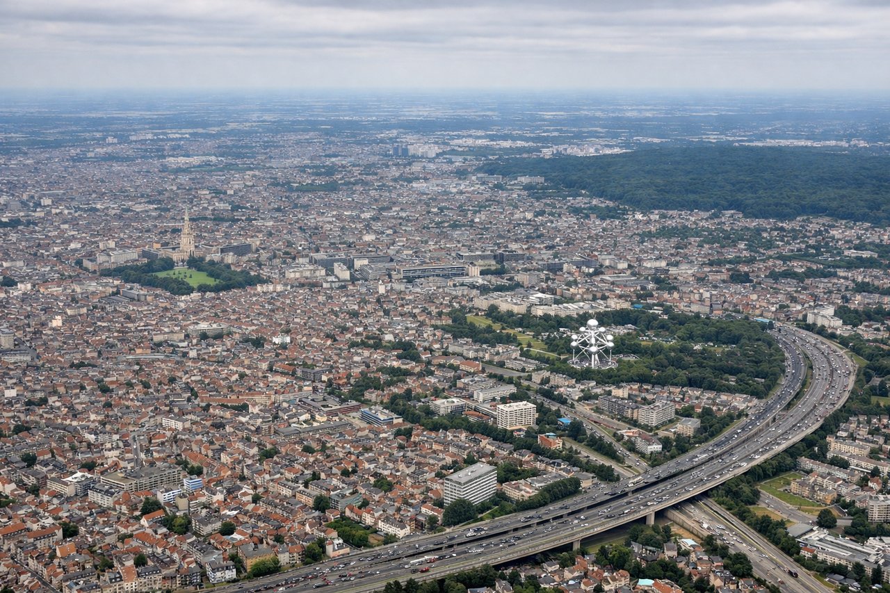 Aerial window seat view during landing at Brussels (left side) — Meuse River (visible as a silvery thread winding through green farmland), Brussels urban sprawl with the Atomium visible on clear days, Flanders agricultural grid (distinctive rectangular field patterns), Scheldt River to the north