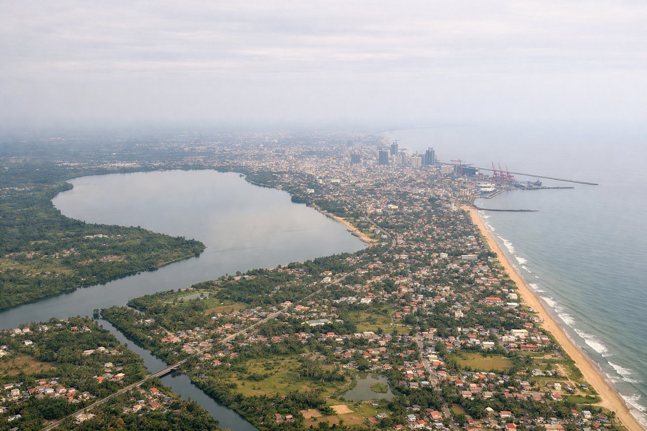 Right window seat view during takeoff from Colombo (CMB) — Colombo city skyline, Colombo Port breakwaters, coastal shoreline south of the airport, Indian Ocean
