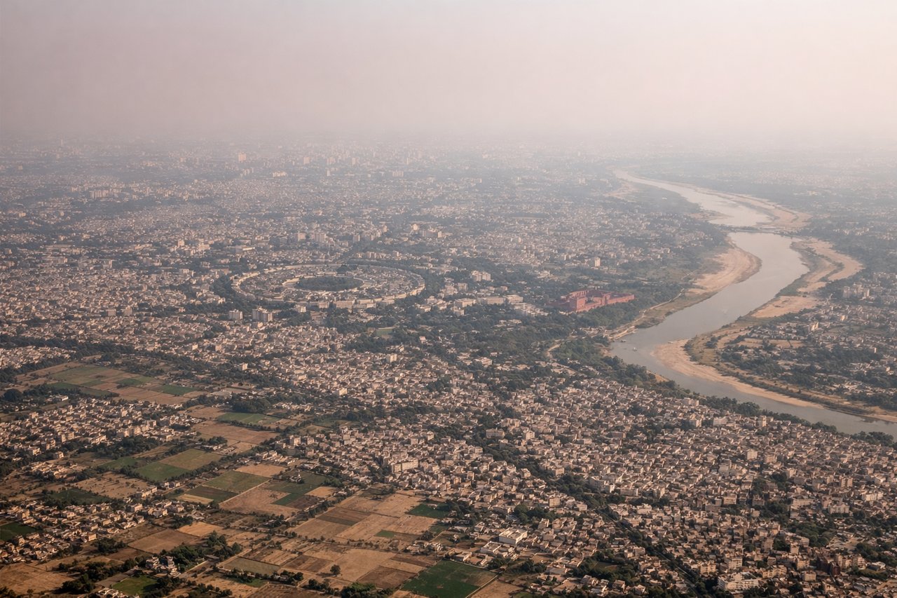 Aerial window seat view during takeoff from Delhi (left side) — Yamuna River bends, Delhi's urban grid, central government district haze, Delhi Ridge forest patch
