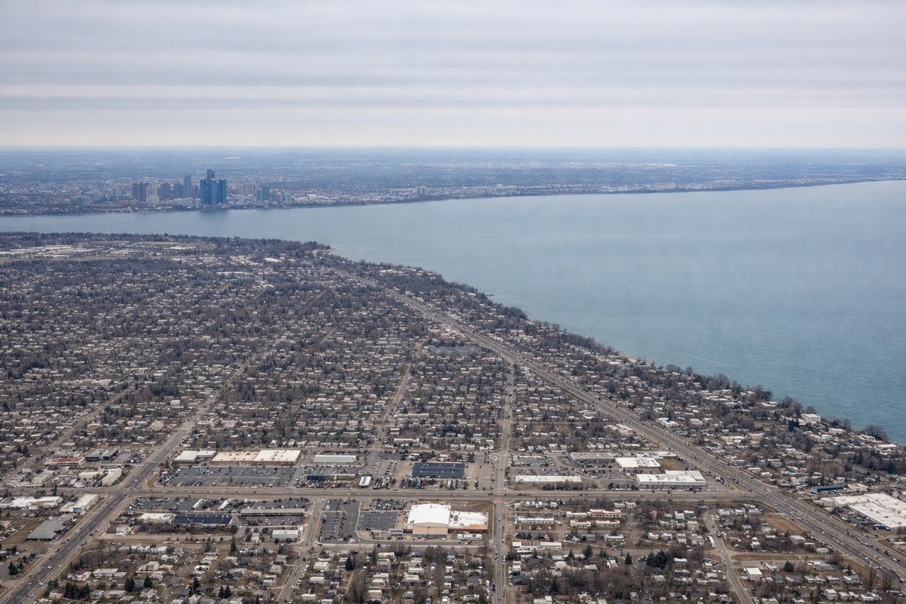 Aerial window seat view during landing at Detroit (right side) — Downtown Detroit skyline, Detroit River, Lake Erie shoreline, Ambassador Bridge