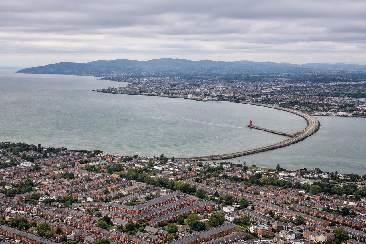 Aerial window seat view during landing at Dublin (left side) — Dublin Bay (recognizable crescent shape), Howth Peninsula (north side of bay), Wicklow Mountains (south and inland, appearing as low ridges on the horizon), Dublin city sprawl and the River Liffey estuary