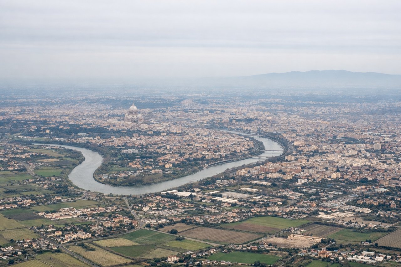 Aerial window seat view during takeoff from Rome (right side) — Tiber River snaking toward central Rome, the dense urban grid of Rome's historic center, the Tyrrhenian Sea coastline to the west, the Alban Hills (Castelli Romani) rising southeast of the city
