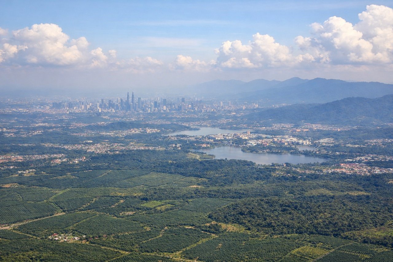 Aerial window seat view during takeoff from Kuala Lumpur (right side) — Putrajaya federal complex and lake, KLIA2 terminal, Titiwangsa Range foothills to the northeast, Sepang palm oil plantation grid patterns