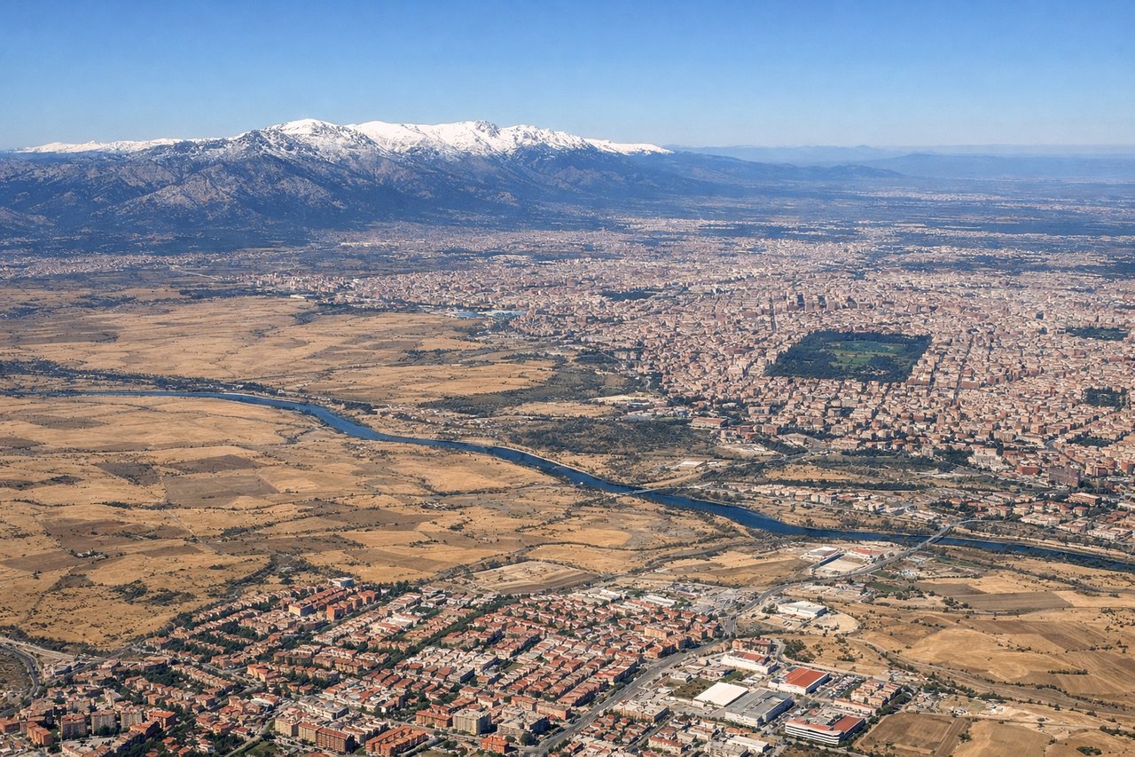 Left window seat view during takeoff from Madrid (MAD) — Sierra de Guadarrama mountain range, Madrid city skyline (including tall towers near Chamartín/Cuatro Torres), Manzanares river valley, Barajas airport's own runway complex receding below