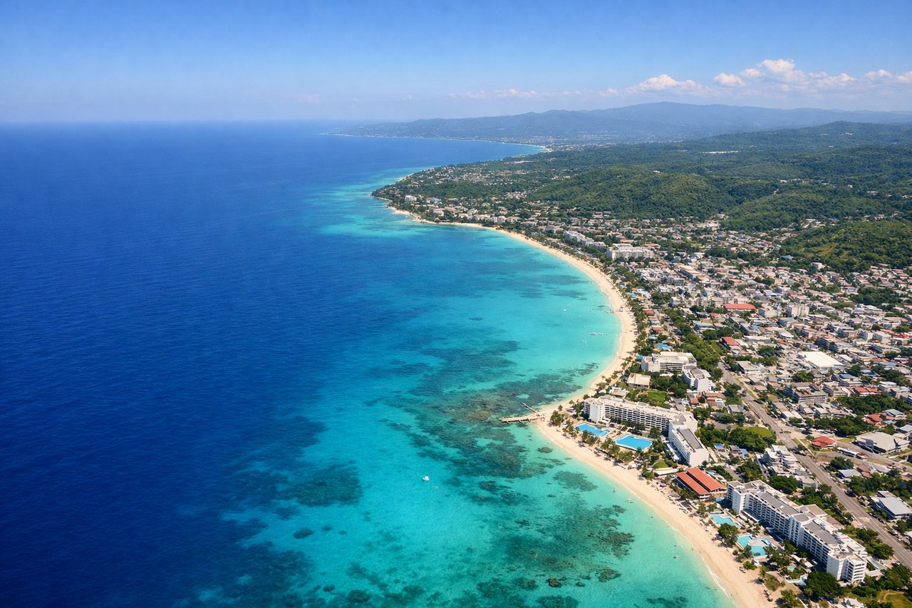 Aerial window seat view during landing at Montego Bay (right side) — Montego Bay's crescent coastline, turquoise Caribbean waters and reef systems, Sangster International Airport runway on the coastal plain, Doctor's Cave Beach area