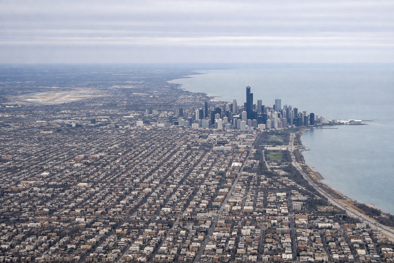 Right window seat view during takeoff from Chicago (ORD) — Chicago downtown skyline (distant, to the south-southeast), Lake Michigan shoreline, O'Hare's runway complex and cargo ramps, western Chicago suburbs and the Des Plaines River corridor