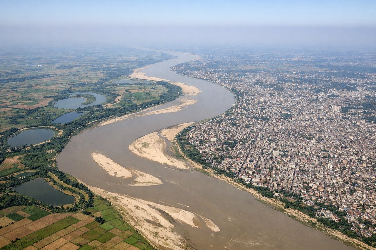 Aerial window seat view during takeoff from Patina (right side) — Ganges River and its braided channels, Patna city grid below, flat Indo-Gangetic Plain extending to the horizon, scattered villages and irrigation ponds across the floodplain