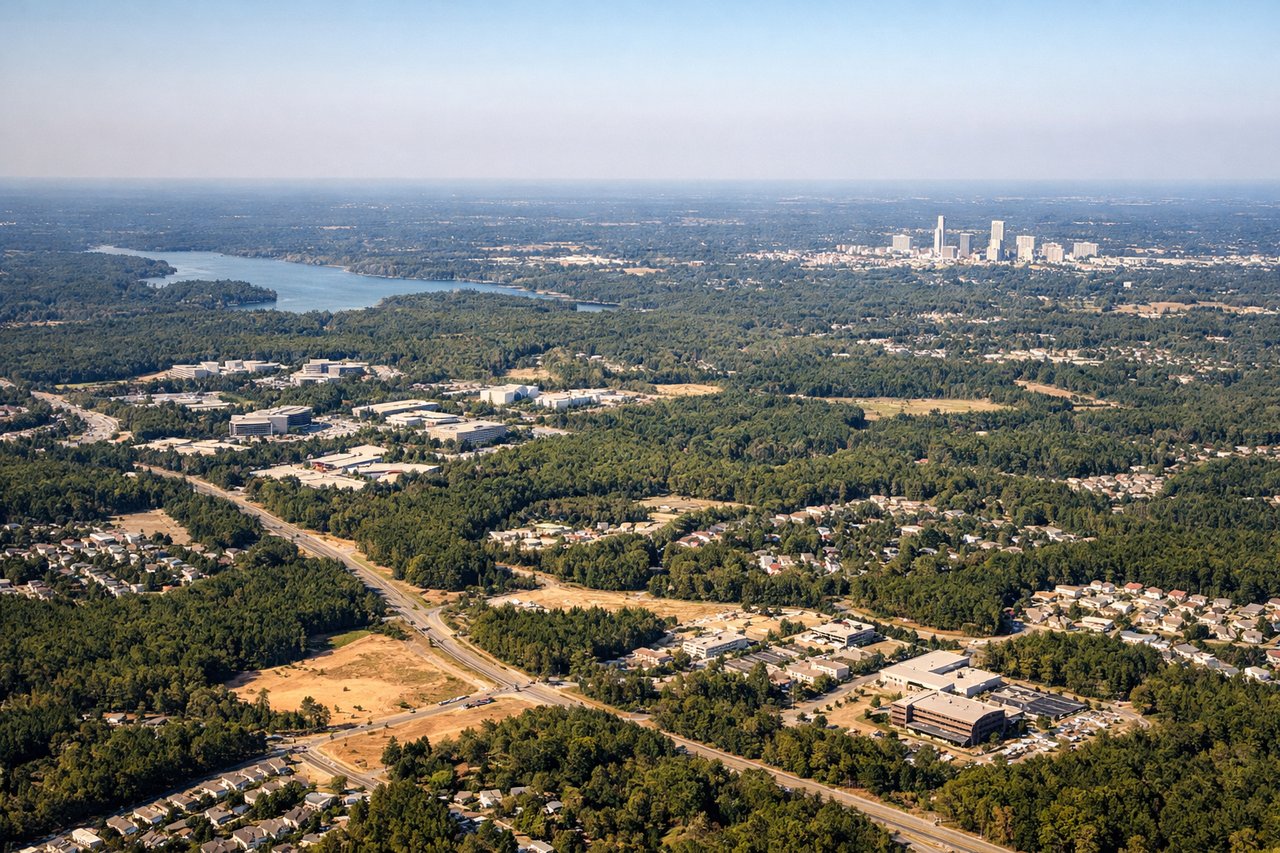Right window seat view during landing at Raleigh-Durham (RDU) — Downtown Raleigh skyline, William B. Umstead State Park lakes, Crabtree Creek corridor, RTP treeline in the far distance