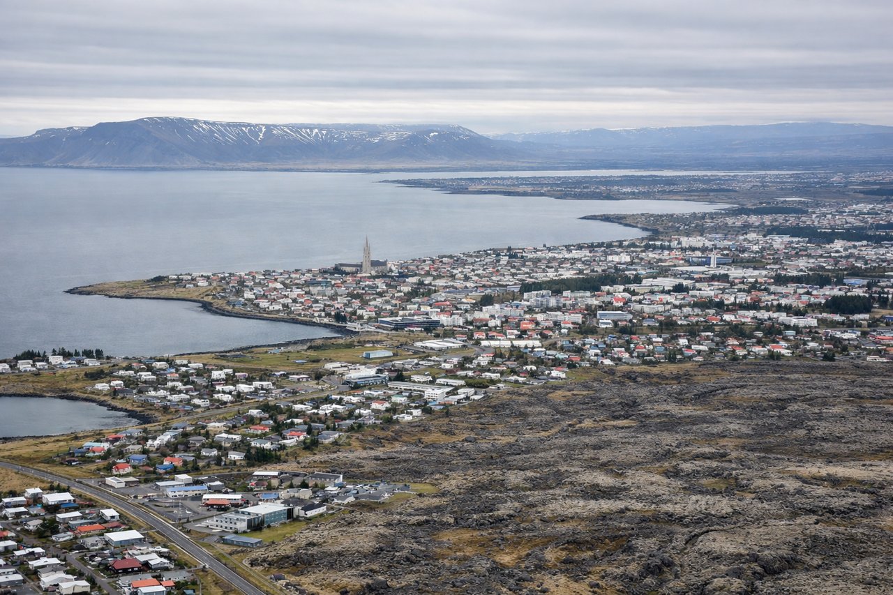 Left window seat view during landing at Reykjavik (RKV) — Faxaflói Bay, Reykjanes Peninsula lava fields, Mount Esja (distant, north-facing slope), coastal settlement clusters