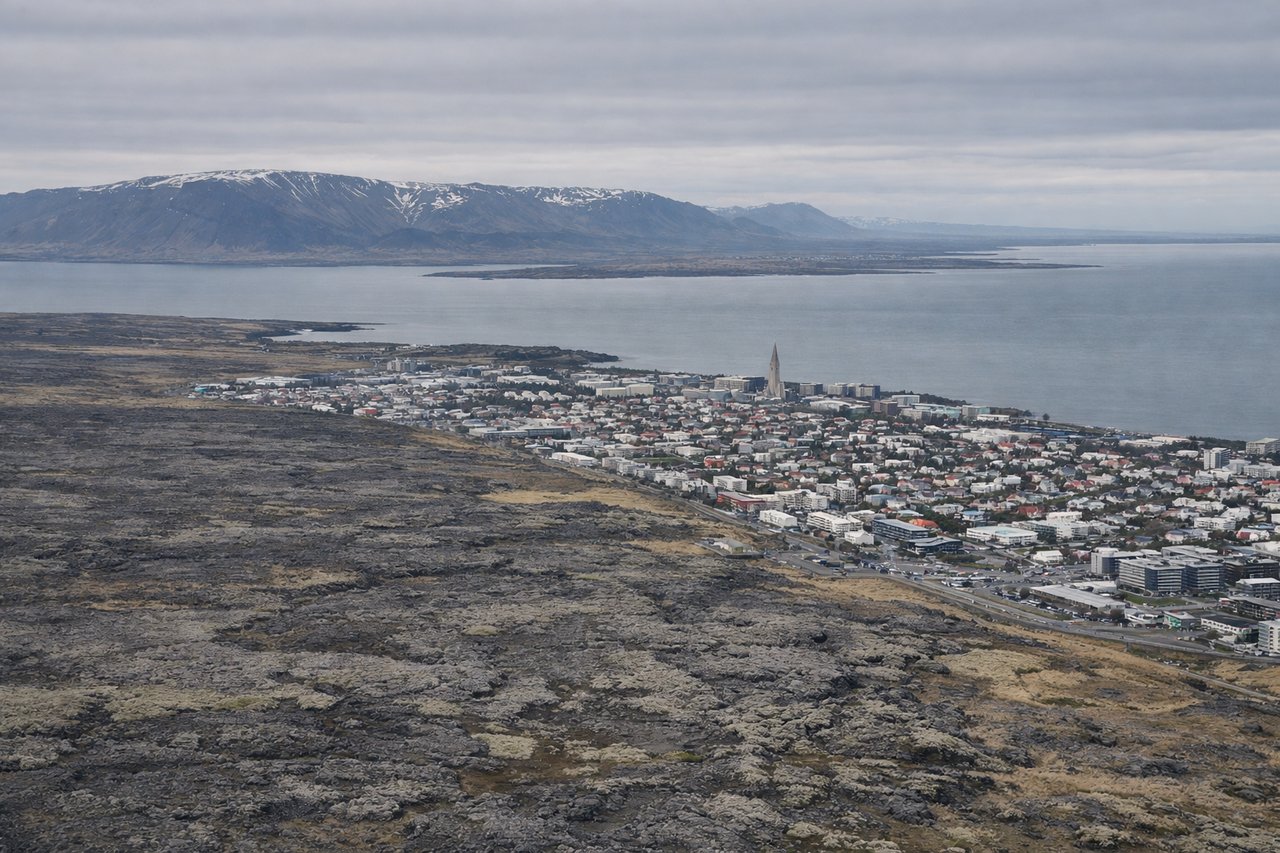 Right window seat view during landing at Reykjavik (RKV) — Faxaflói Bay, Reykjanes Peninsula lava fields, Mount Esja (distant, north-facing slope), coastal settlement clusters