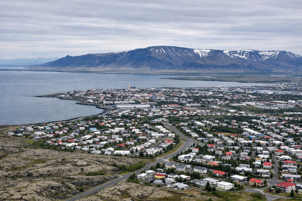 Left window seat view during takeoff from Reykjavik (RKV) — Reykjanes Peninsula geothermal area (steam vents and hot springs visible as white plumes), Fagradalsfjall volcanic region, Atlantic coastline with black sand beaches, distant Snæfellsjökull glacier on the horizon to the northwest
