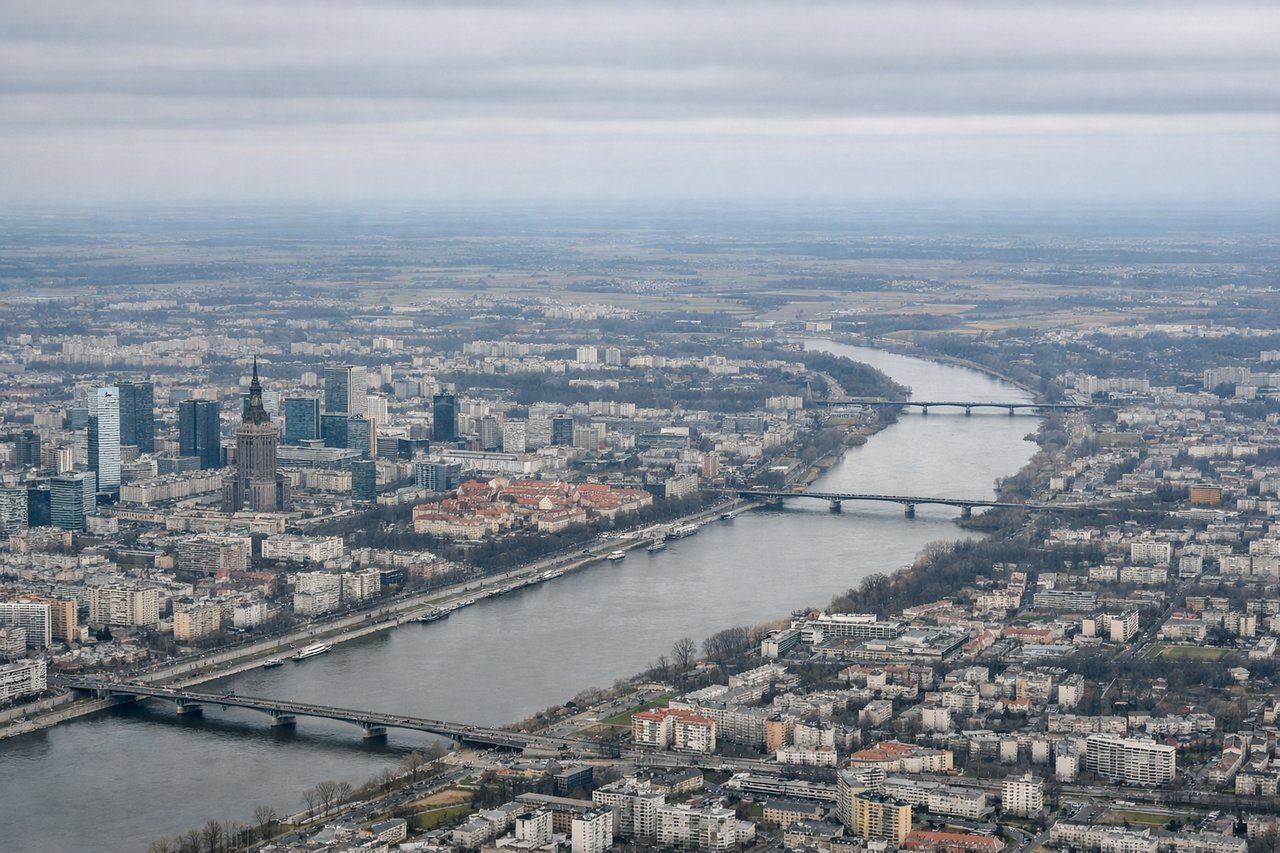 Right window seat view during takeoff from Warsaw (WAW) — Vistula River (multiple bends visible), Warsaw city center and Old Town district, Praga district across the river, flat agricultural plains extending to the northern horizon